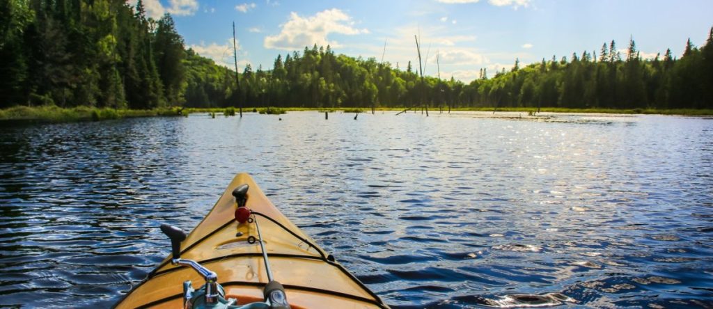 Matthew Davies image of a person on a kayak on a lake surrounded by beautiful mountains and blue sky.